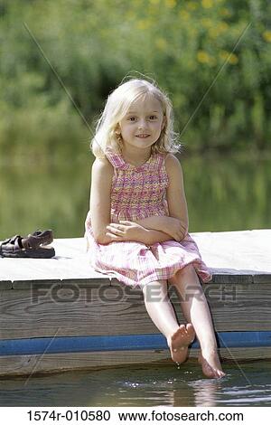 Stock Image - Portrait of a girl sitting at the edge of a pier. Fotosearch