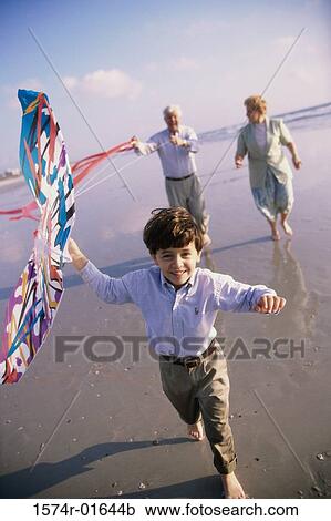 Stock Image - Portrait of a grandson flying a kite at the beach with his grandparents. Fotosearch