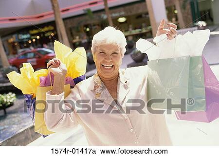 Stock Image - Portrait of a senior woman standing in a shopping mall with shopping bags. Fotosearch
