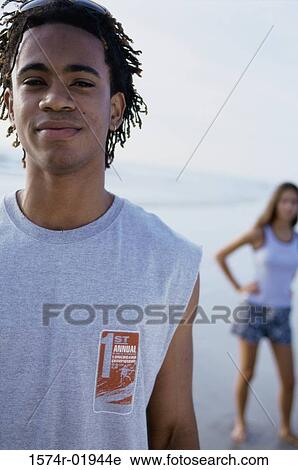 Portrait of a teenage boy standing at the beach with a teenage girl behind him View Large Photo Image Stock Image - Portrait of a teenage boy standing at the beach with a teenage girl behind him. Fotosearch