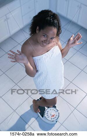 Stock Image - Portrait of a teenage girl standing on a weighing scale. Fotosearch