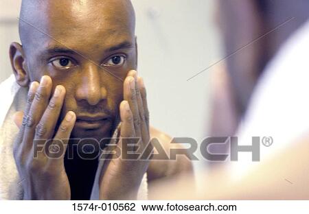 Portrait of a young man touching his face looking in a mirror View Large Photo Image Stock Image - Portrait of a young man touching his face looking in a mirror. Fotosearch