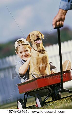 Stock Image - Portrait of boy sitting in a toy wagon with his dog. Fotosearch