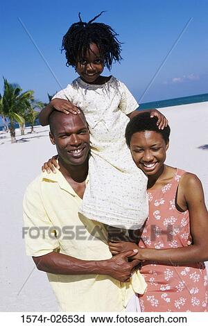 Stock Image - Portrait of parents carrying their daughter on their shoulders. Fotosearch