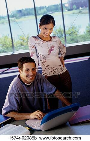 Stock Image - Portrait of young man in front of a laptop with a teenage girl behind him. Fotosearch