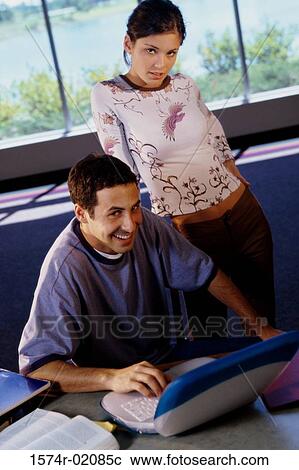 Portrait of young man in front of a laptop with a teenage girl behind him View Large Photo Image Stock Image - Portrait of young man in front of a laptop with a teenage girl behind him. Fotosearch