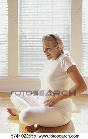 Pregnant woman sitting on the floor touching her abdomen View Large Photo Image Stock Image - Pregnant woman sitting on the floor touching her abdomen. Fotosearch