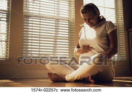 Pregnant woman sitting on the floor touching her abdomen View Large Photo Image Stock Image - Pregnant woman sitting on the floor touching her abdomen. Fotosearch