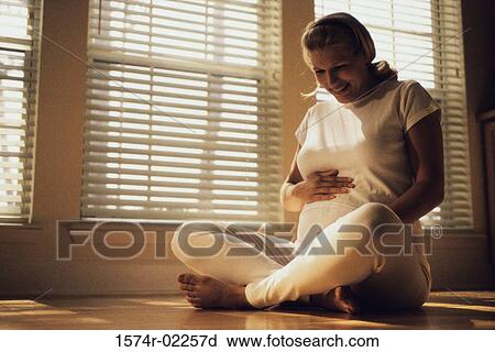 Pregnant woman sitting on the floor touching her abdomen View Large Photo Image Stock Image - Pregnant woman sitting on the floor touching her abdomen. Fotosearch