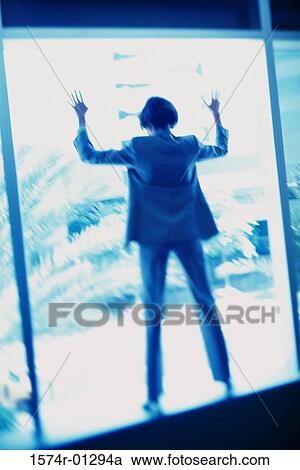 Stock Image - Rear view of a businesswoman leaning against a window. Fotosearch