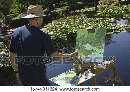 Picture - Rear view of a young man painting with a paintbrush. Fotosearch