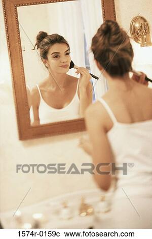Stock Image - Rear view of young woman in a bathroom applying blush. Fotosearch