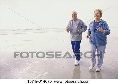 Stock Image - Senior couple jogging at the beach. Fotosearch