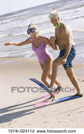 Stock Image - Senior couple walking on the beach wearing snorkeling gear. Fotosearch