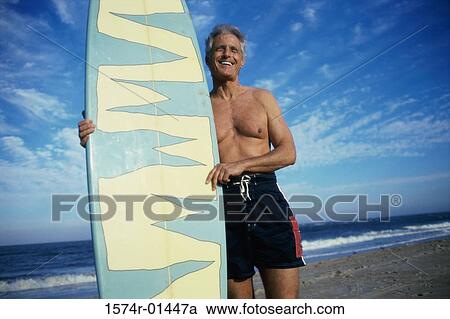 Stock Image - Senior man holding a surfboard. Fotosearch