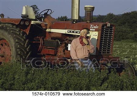Stock Photo - Senior man leaning against a tractor. Fotosearch