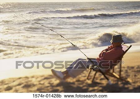 Senior man sitting on a deck chair with a fishing rod View Large Photo Image Stock Image - Senior man sitting on a deck chair with a fishing rod. Fotosearch
