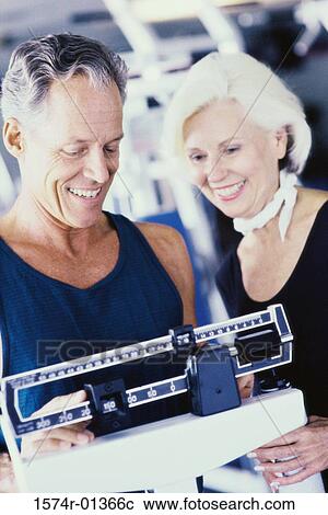 Stock Image - Senior man standing on a weighing scale with a senior woman beside him. Fotosearch