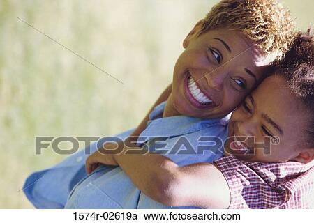 Stock Image - Side profile of a daughter riding piggyback on her mother. Fotosearch