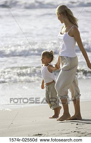 Stock Image - Side profile of a mother and her daughter walking on the beach. Fotosearch
