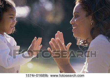Stock Image - Side profile of a mother playing pattycake with her daughter. Fotosearch