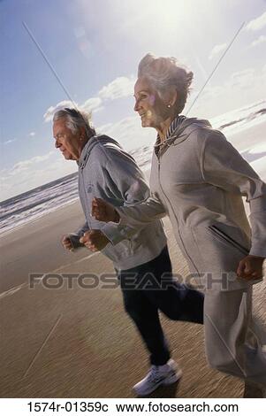 Stock Image - Side profile of a senior couple running at the beach. Fotosearch