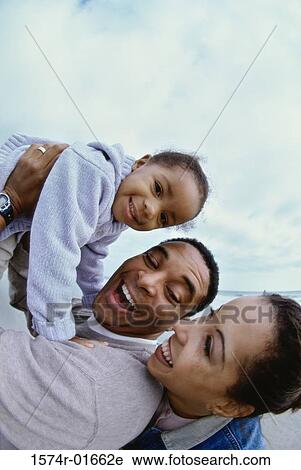 Stock Image - Side profile of parents carrying their daughter. Fotosearch