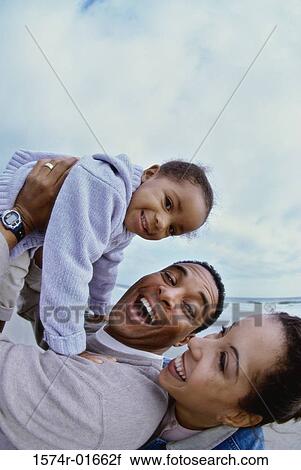 Stock Image - Side profile of parents carrying their daughter. Fotosearch
