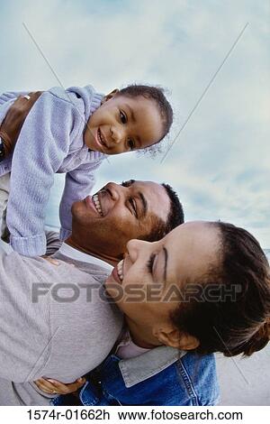 Stock Image - Side profile of parents carrying their daughter. Fotosearch