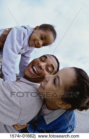 Stock Image - Side profile of parents carrying their daughter. Fotosearch