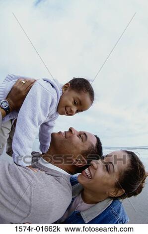 Stock Image - Side profile of parents carrying their daughter. Fotosearch