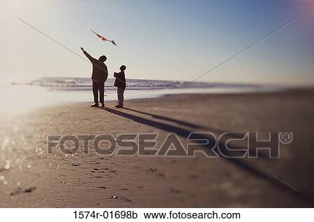 Stock Image - Silhouette of a father and son flying a kite on the beach. Fotosearch