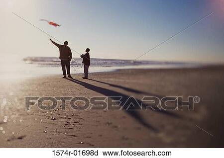 Stock Image - Silhouette of a father and son flying a kite on the beach. Fotosearch