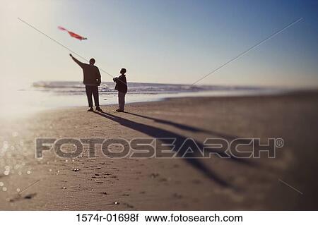 Stock Image - Silhouette of a father and son flying a kite on the beach. Fotosearch