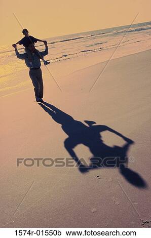 Stock Image - Silhouette of a man carrying his son on his shoulders at the beach. Fotosearch