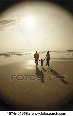 Stock Image - Silhouette of parents walking on the beach with their child. Fotosearch