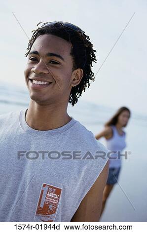 Stock Image - Teenage boy standing at the beach with a teenage girl behind him. Fotosearch