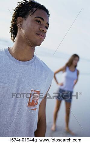 Teenage boy standing at the beach with a teenage girl behind him View Large Photo Image Stock Image - Teenage boy standing at the beach with a teenage girl behind him. Fotosearch