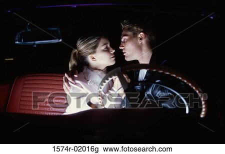 Stock Image - Teenage couple sitting in a car looking at each other. Fotosearch