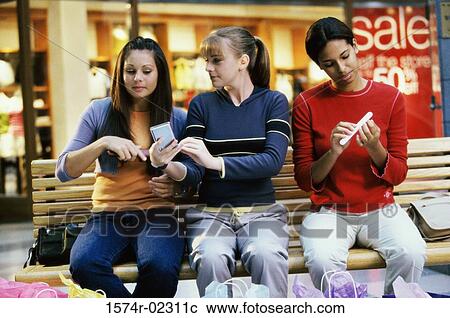 Three teenage girls sitting on a bench in a shopping mall applying make-up View Large Photo Image Stock Image - Three teenage girls sitting on a bench in a shopping mall applying make-up. Fotosearch