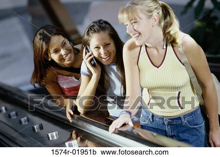 Stock Image - Three teenage girls standing on an escalator. Fotosearch