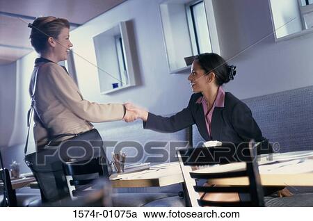 Stock Image - Two businesswomen shaking hands in a restaurant. Fotosearch