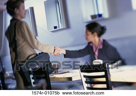 Stock Image - Two businesswomen shaking hands in restaurant. Fotosearch