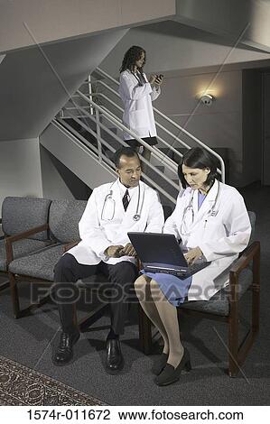 Two doctors sitting in front of a laptop View Large Photo Image Stock Image - Two doctors sitting in front of a laptop. Fotosearch