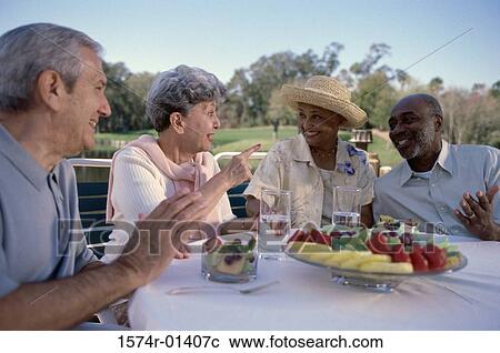 Stock Image - Two senior couples seated at a table talking. Fotosearch