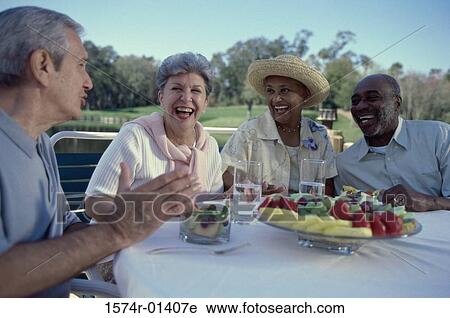 Stock Image - Two senior couples seated at a table talking. Fotosearch