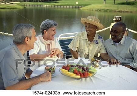 Stock Image - Two senior couples sitting at an outdoor restaurant. Fotosearch