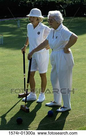 Stock Image - Two senior women standing on a golf course holding golf clubs. Fotosearch