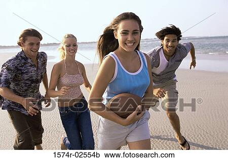 Stock Image - Two teenage couples playing football on the beach. Fotosearch