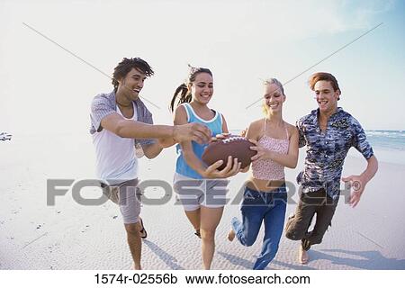 Stock Image - Two teenage couples playing football on the beach. Fotosearch